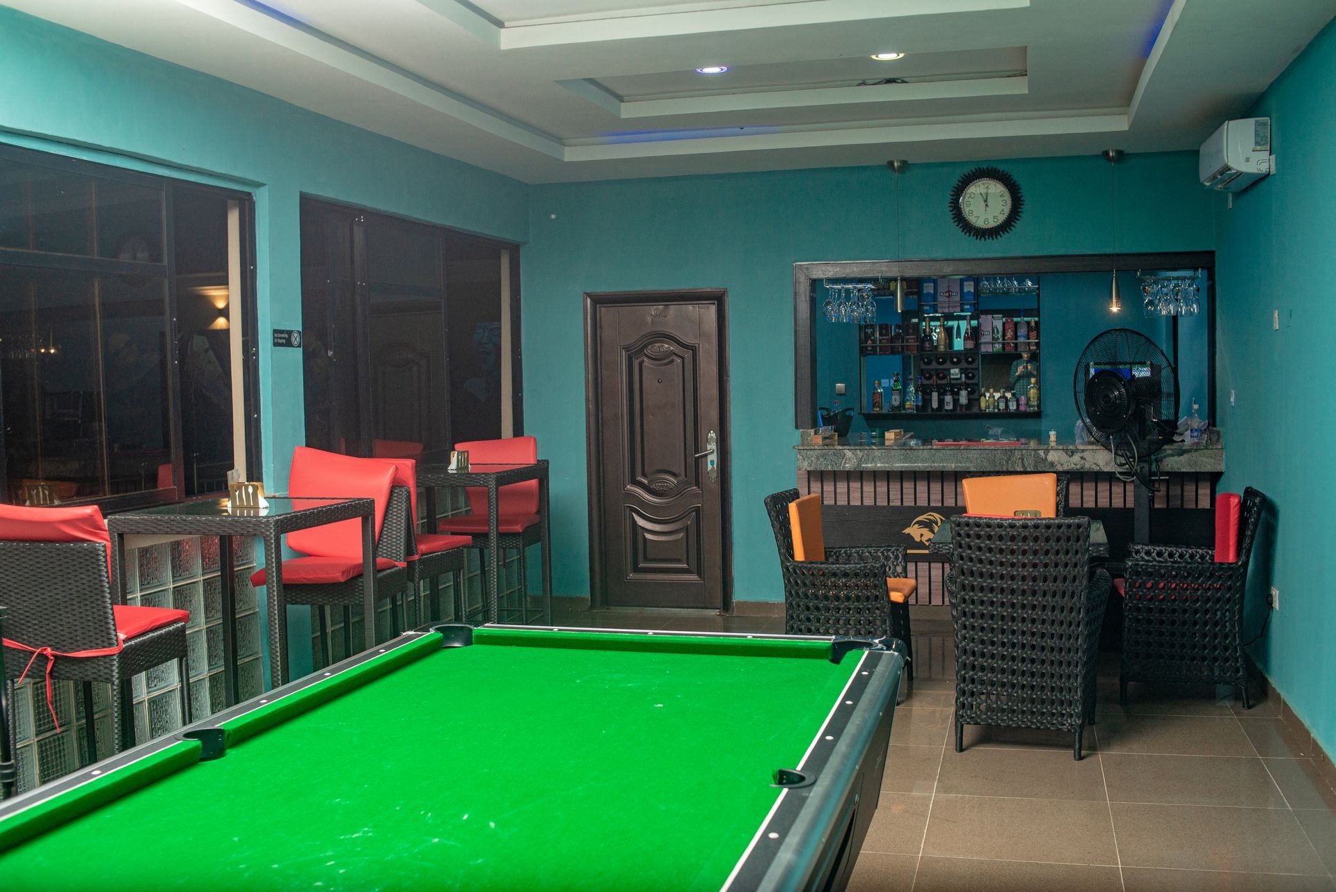 Bar area with pool table, wicker chairs, red bar stools, and a shelf with bottles.