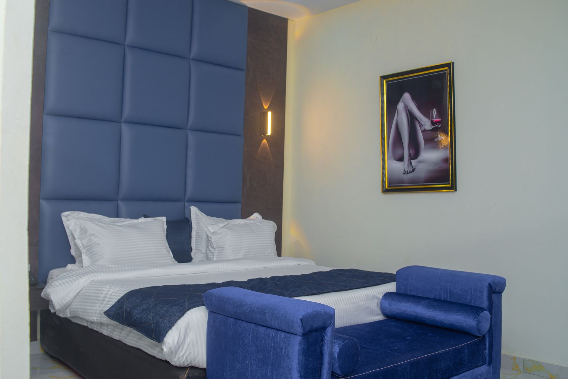 Modern bedroom with blue padded headboard, white bedding, and framed art on the wall.