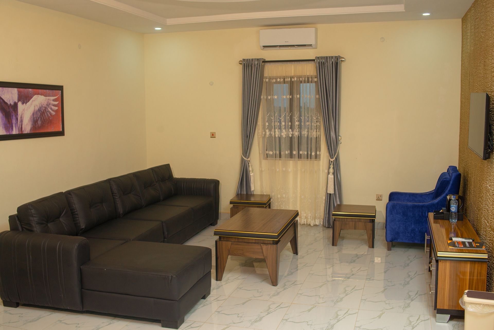 Modern living room with black sofa, wooden furniture, blue chair, and window with curtains.