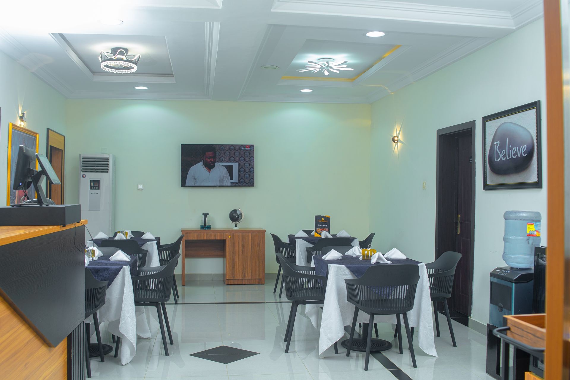 Modern dining room with neatly set tables, TV on wall, and a water dispenser.